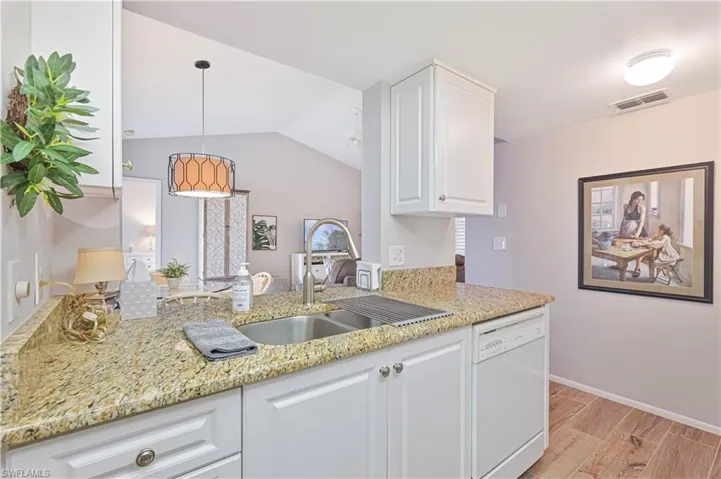 Kitchen featuring white cabinets, light stone counters, a sink, and white dishwasher