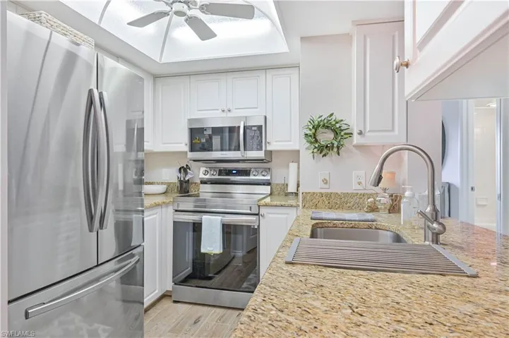 Kitchen featuring a sink, appliances with stainless steel finishes, a ceiling fan, white cabinets, and light wood-style floors