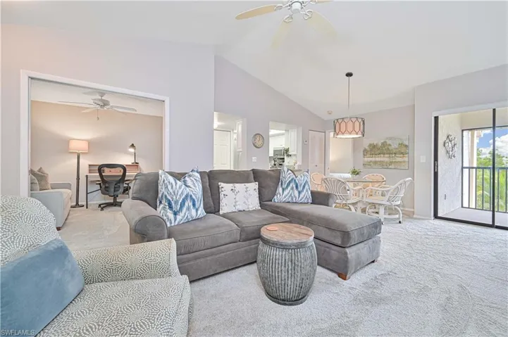 Carpeted living area featuring lofted ceiling, baseboards, and ceiling fan