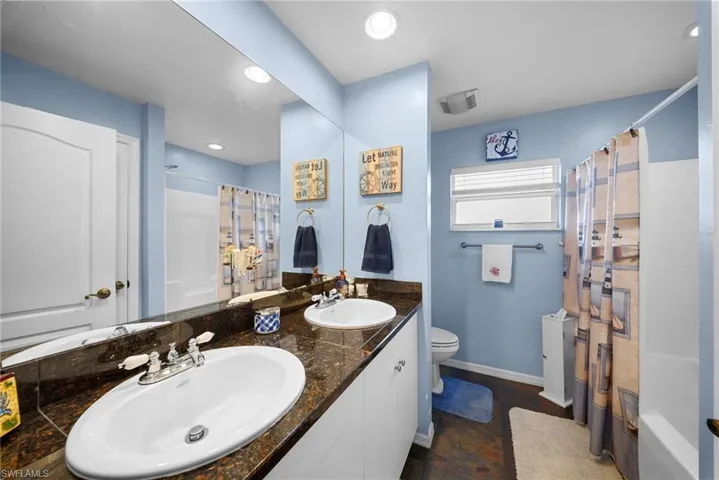 Bathroom featuring a dual-sink vanity with white cabinetry, dark stone countertops, undermount sinks, chrome fixtures, and a wall-to-wall mirror