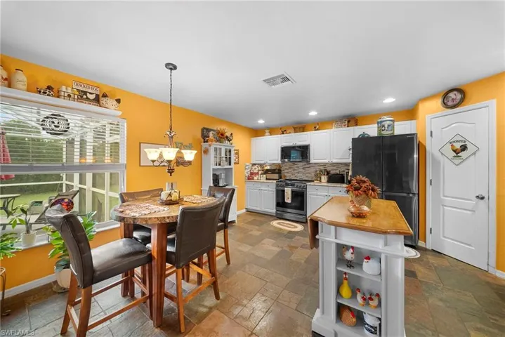 Kitchen featuring white shaker-style cabinetry, a multi-tone slate tile floor, stone-composite backsplash, and a central workstation island with a wood-finish surface