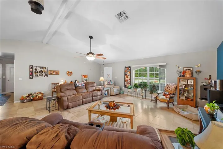 Living area featuring vaulted ceilings with exposed beams, large format neutral floor tiling, and an arched window