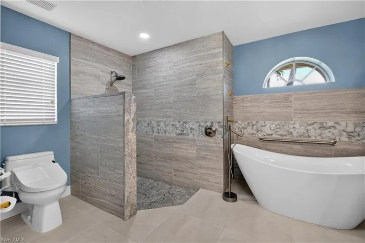 Walk-in shower with tiled walls and floor, free-standing soaking tub with floor-mounted faucet, and a half-moon window