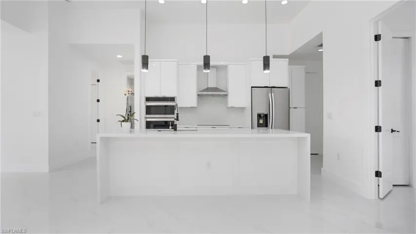 Kitchen with appliances with stainless steel finishes, wall chimney exhaust hood, modern cabinets, white cabinets, and light countertops