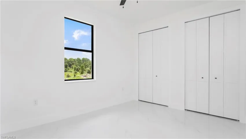 Unfurnished bedroom featuring multiple closets, light marble finish flooring, and ceiling fan