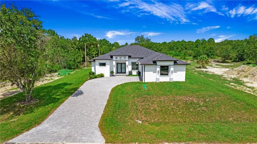 View of front of home featuring decorative driveway, a front lawn, stucco siding, french doors, and a forest view