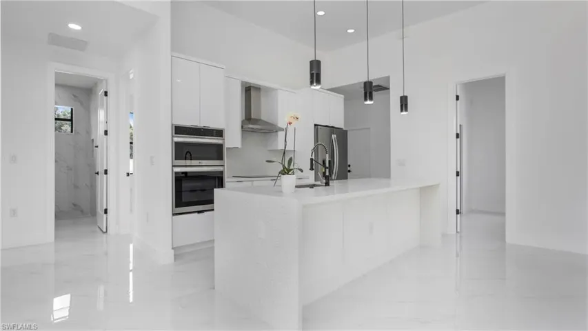Kitchen featuring modern cabinets, appliances with stainless steel finishes, wall chimney range hood, light marble finish floors, and recessed lighting