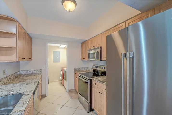 Kitchen with stainless steel appliances, light brown cabinetry, light stone counters, light tile floors, and washer and clothes dryer