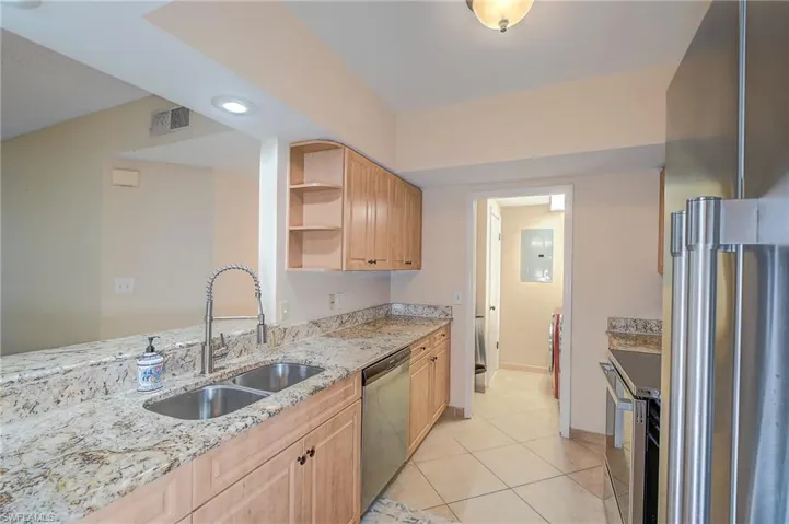 Kitchen with light stone countertops, stainless steel appliances, light tile floors, sink, and light brown cabinetry