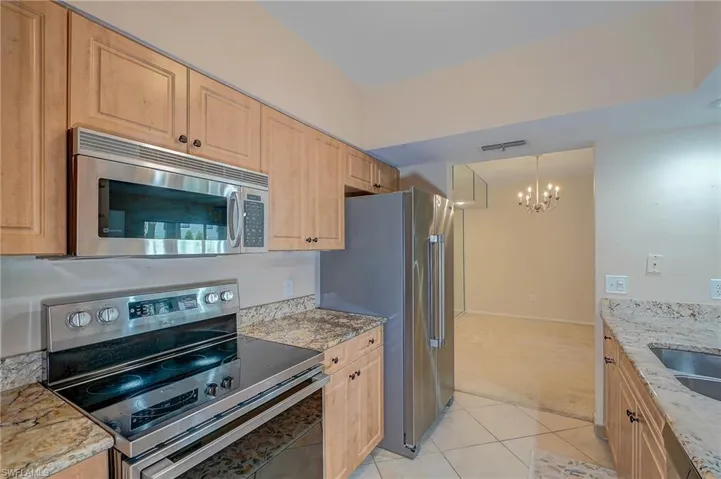 Kitchen with an inviting chandelier, light stone counters, stainless steel appliances, hanging light fixtures, and light tile floors