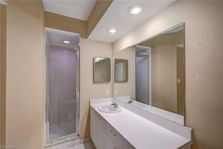 Bathroom featuring tile floors, an enclosed shower, a textured ceiling, and vanity with extensive cabinet space