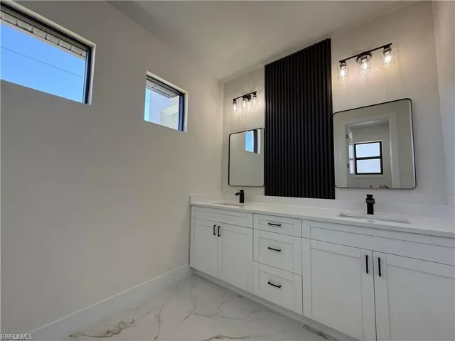 Bathroom with double vanity and light marble finish flooring