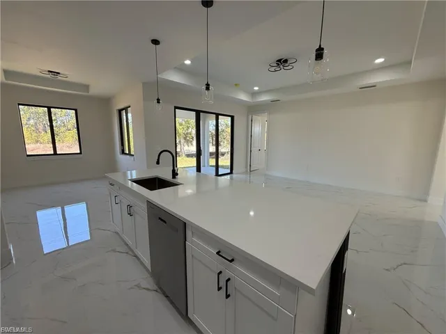 Kitchen with open floor plan, a tray ceiling, a kitchen island with sink, hanging light fixtures, and dishwasher