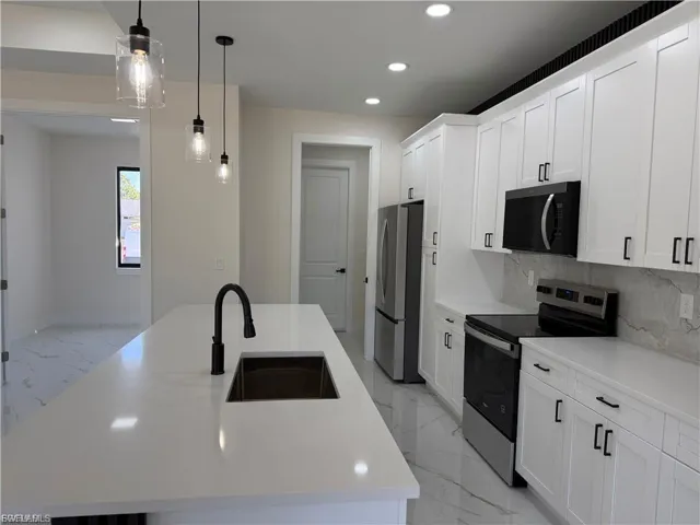Kitchen with stainless steel appliances, an island with sink, white cabinetry, and light marble finish flooring