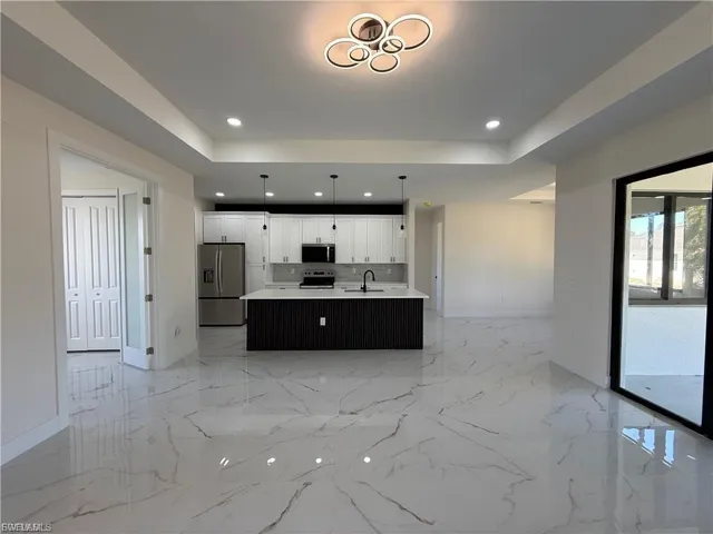 Kitchen featuring open floor plan, stainless steel appliances, white cabinets, an island with sink, and pendant lighting