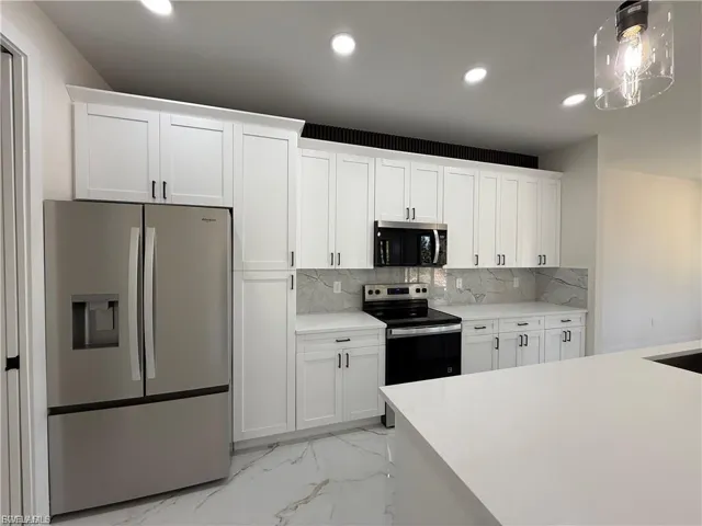 Kitchen featuring stainless steel appliances, light marble finish floors, and white cabinetry