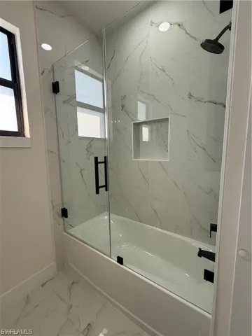 Bathroom with bath / shower combo with glass door and light marble finish floors