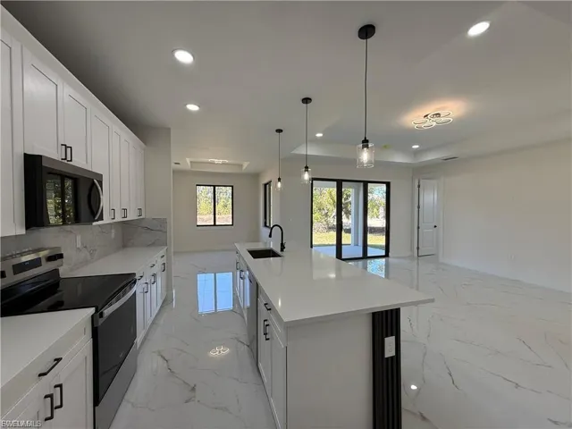 Kitchen with stainless steel appliances, white cabinetry, a center island with sink, open floor plan, and pendant lighting