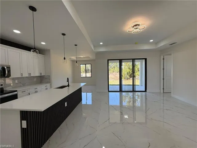 Kitchen featuring stainless steel appliances, an island with sink, white cabinets, light stone countertops, and a raised ceiling