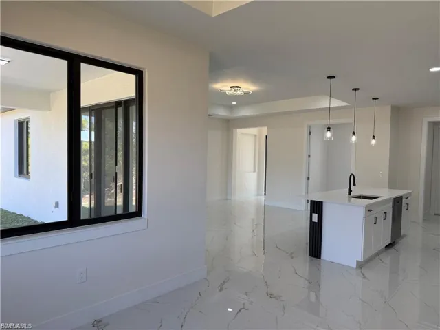 Kitchen featuring pendant lighting, an island with sink, light stone counters, white cabinetry, and stainless steel dishwasher