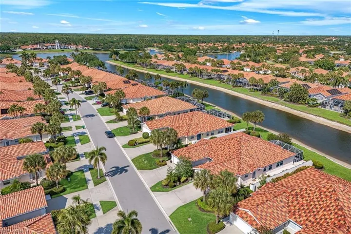 Aerial view of the property and its surrounding neighborhood, featuring red tile roofs, mature palm trees, and a canal running alongside properties