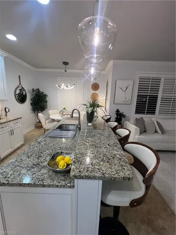 Kitchen with dark stone counters, a breakfast bar, ornamental molding, white cabinets, and a center island with sink
