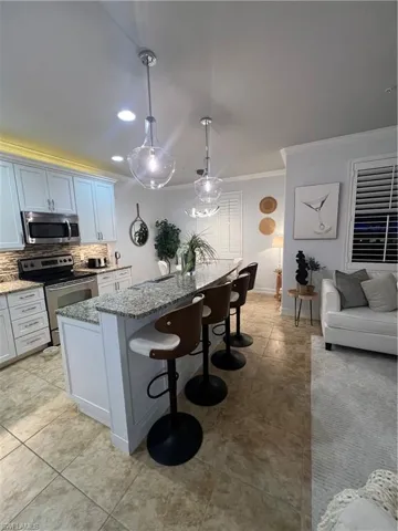 Kitchen with a breakfast bar area, range, light stone countertops, crown molding, and backsplash
