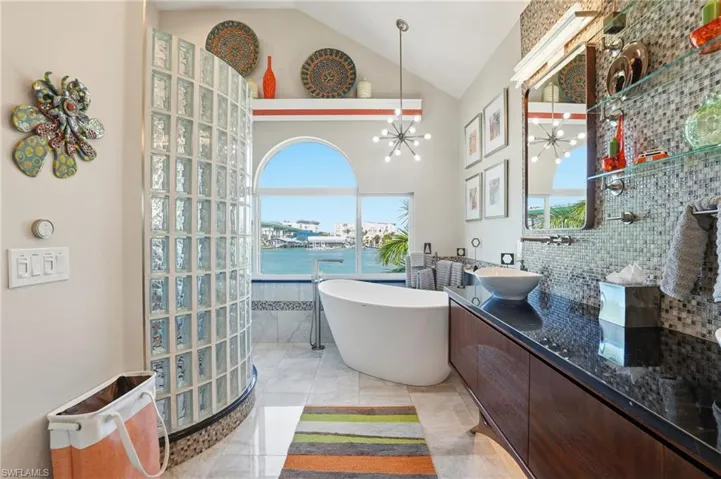 Bathroom featuring vanity, vaulted ceiling, tile walls, a soaking tub, and a water view - Virtually Edited Image
