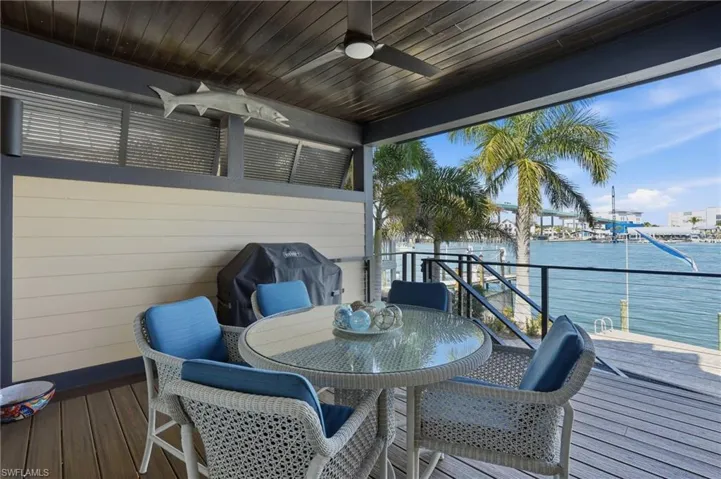 Wooden deck featuring a ceiling fan, area for grilling, outdoor dining space, and a water view - Virtually Edited Image