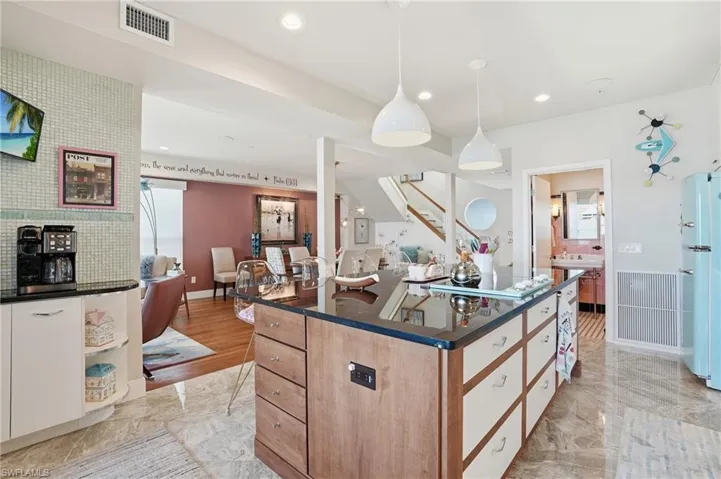 Kitchen featuring a kitchen island, decorative light fixtures, freestanding refrigerator, light marble finish floors, and open floor plan - Virtually Edited Image