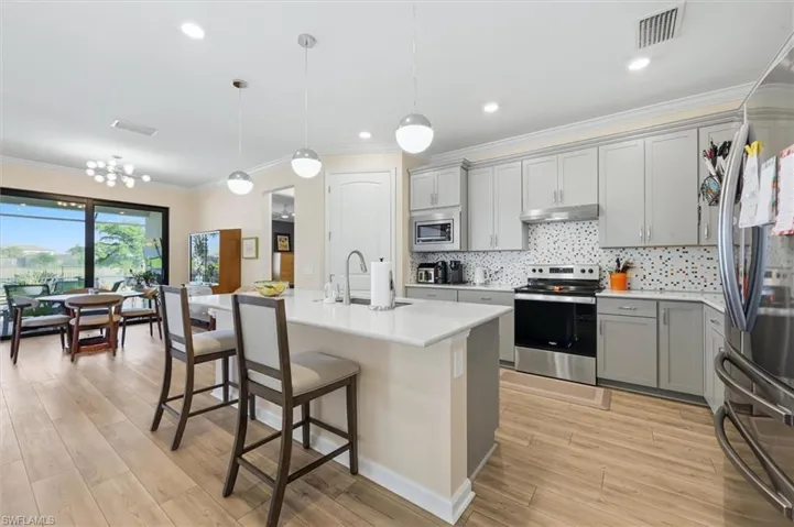 Kitchen featuring a central island with a quartz countertop, light grey shaker-style cabinetry, mosaic tile backsplash, stainless steel appliances, and wood-finish flooring