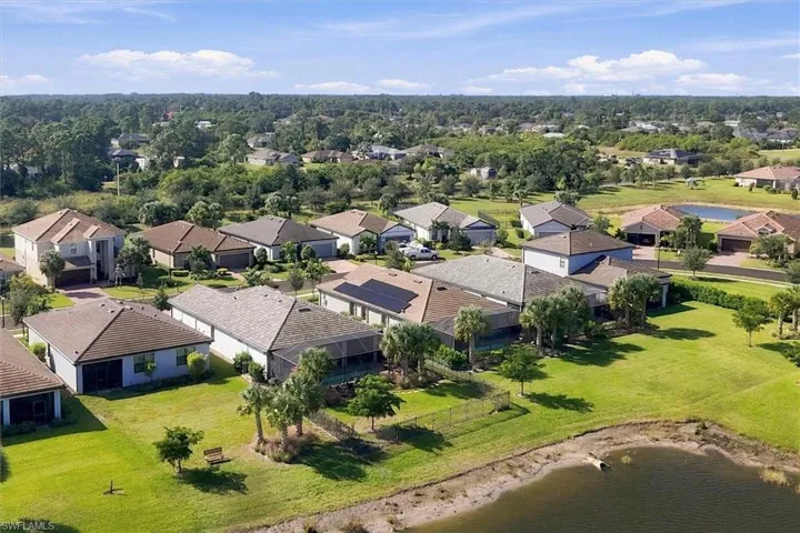 Aerial perspective of a residential community featuring single-family homes with hip roofs, solar panel installations, screened-in lanais, and expansive turf lawns situated on a waterfront lot