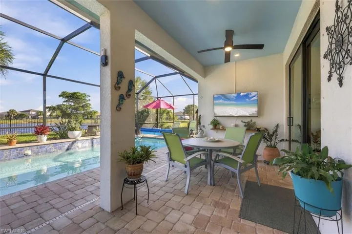 Covered lanai featuring paver flooring, a ceiling fan, and an enclosed screen cage housing an in-ground pool with a decorative tiled waterline