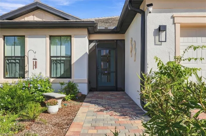 Stucco exterior facade featuring a multi-tone paver walkway, dark metal-framed windows, and an enclosed entryway