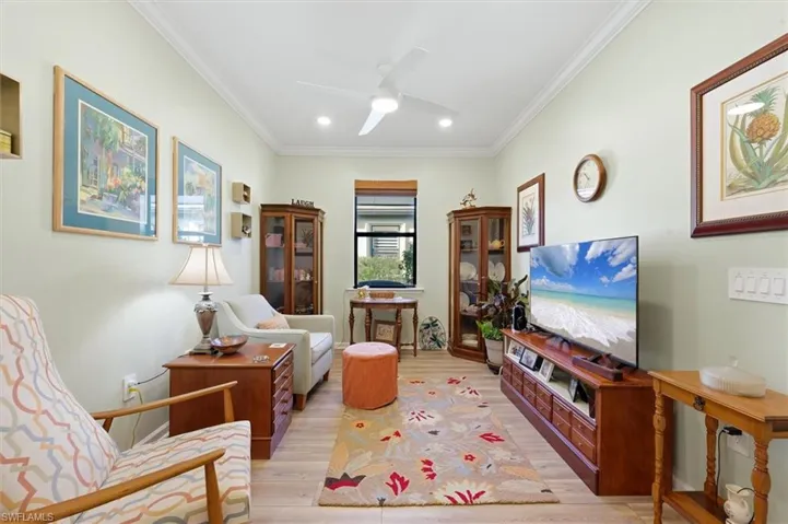 Room featuring wood-finish flooring, crown molding, a central ceiling fan with integrated lighting, and recessed overhead illumination