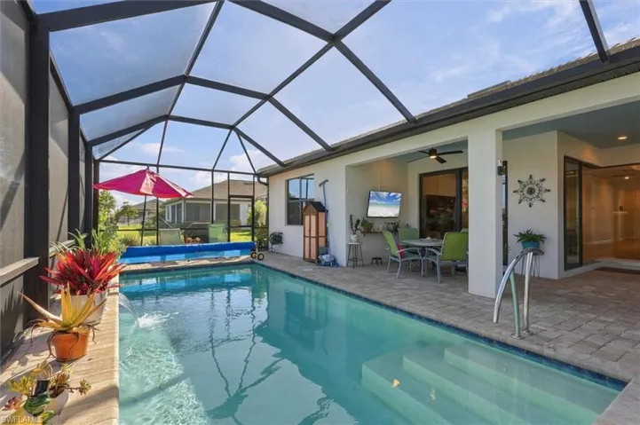 Screen-enclosed swimming pool featuring a tanning ledge, water feature, and brick-paver deck