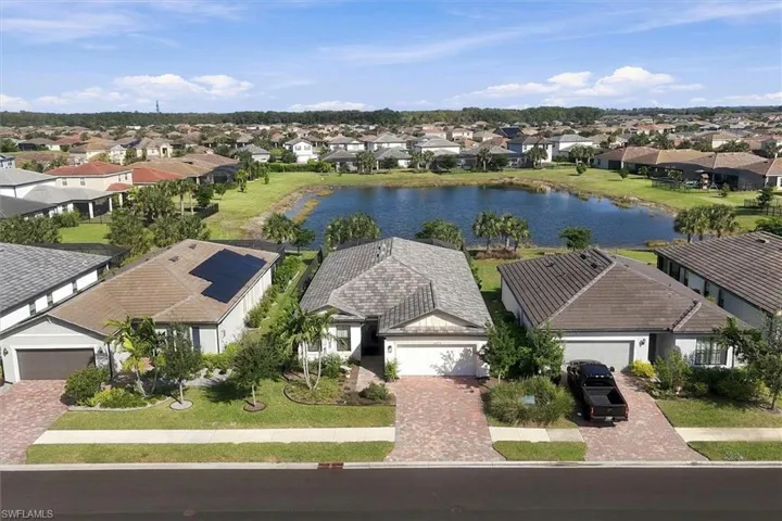Aerial perspective featuring residences with paver driveways, hip-style roofing, and integrated solar panels, oriented toward a community pond and green space