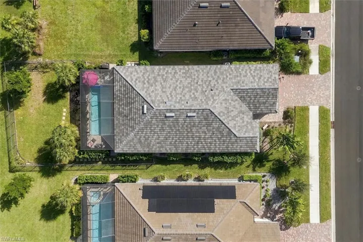 Aerial view of residential property featuring a screened-in swimming pool, shingled roofing, manicured lawn, and paved driveway