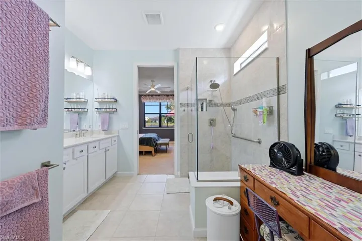Bathroom featuring white dual-sink vanity, glass-enclosed walk-in shower with tiled surround, and ceramic tile flooring