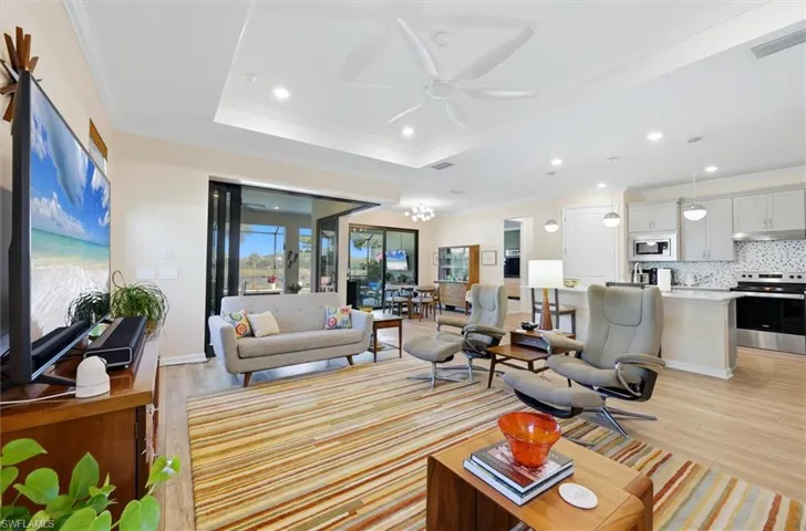 Open-concept living space featuring a tray ceiling, recessed lighting, white ceiling fan, wood-finish flooring, and multi-panel sliding glass doors