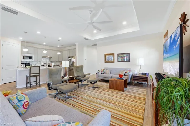 Tray ceiling with recessed lighting, ceiling fan, neutral wall finishes, wood-finish flooring, and kitchen featuring an island with pendant lighting