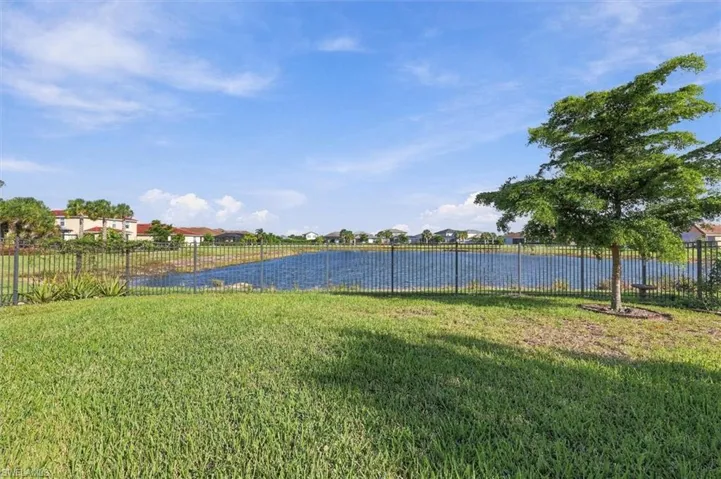 Backyard featuring a grass lawn, metal perimeter fencing, a water feature, and a mature tree