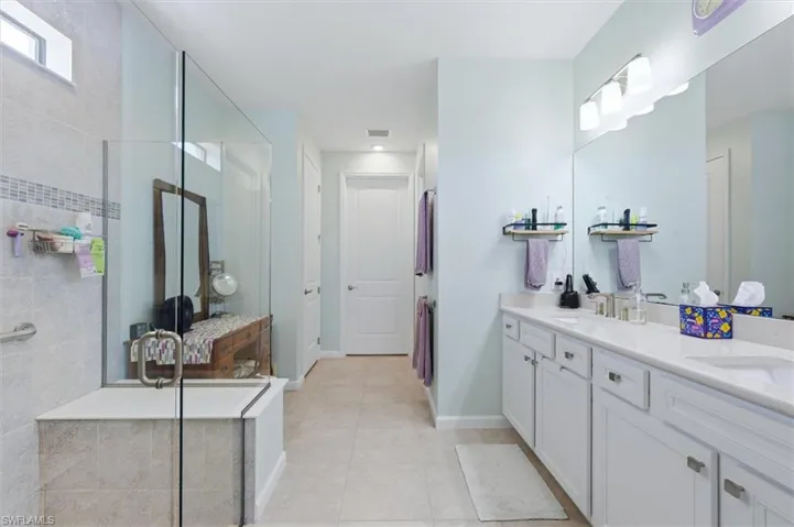 Double vanity featuring white cabinetry, solid-surface countertops, and a full-width wall mirror, paired with a glass-enclosed walk-in shower featuring tile surround