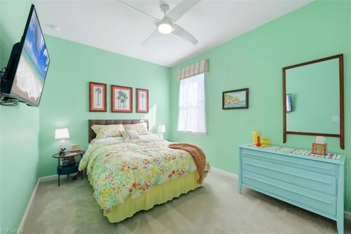 Room featuring neutral-toned carpeting, high ceilings, a white ceiling fan with integrated lighting, and a single window with a fabric valance