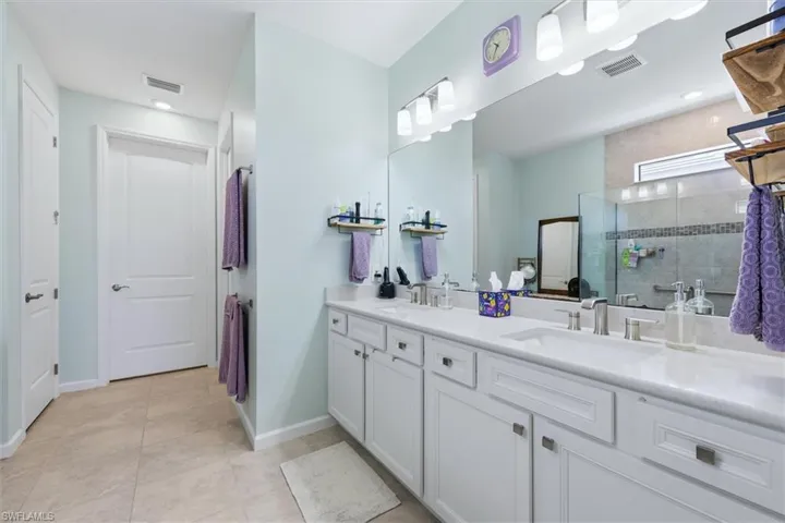 Dual-sink vanity with white cabinetry, light-toned stone countertop, walk-in glass-enclosed shower, and large wall-to-wall mirror