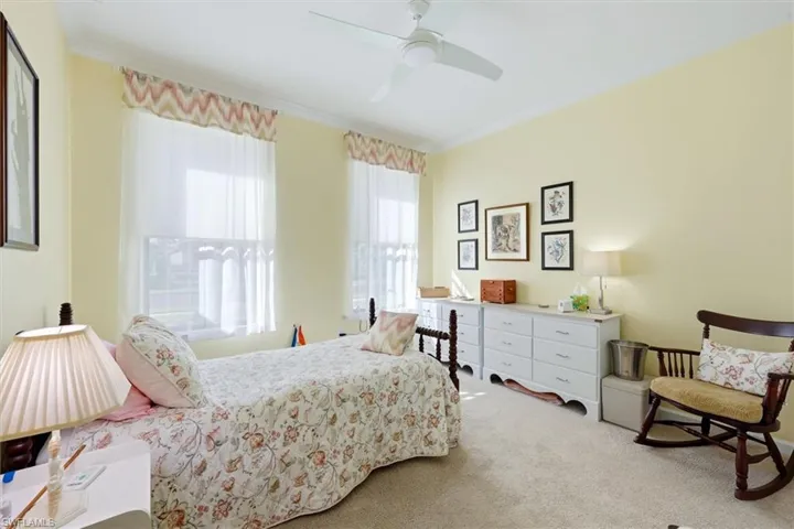 Neutral-toned room featuring neutral wall-to-wall carpeting, crown molding, two large windows with patterned valances, and a ceiling fan
