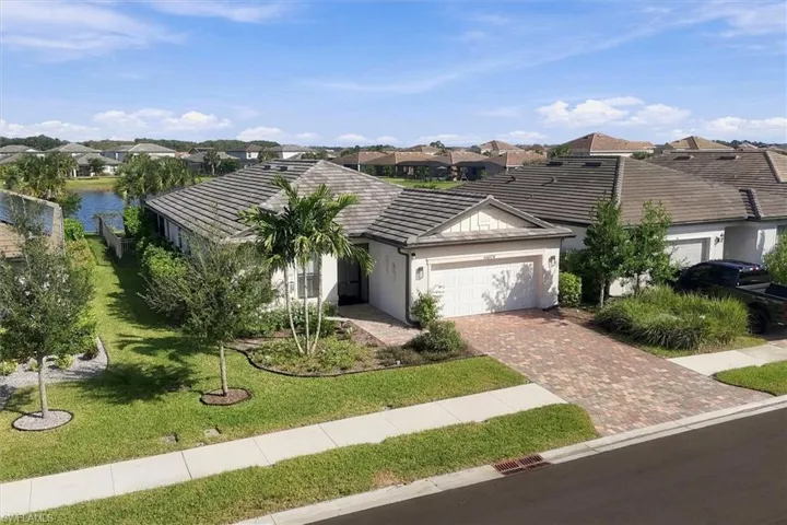 Single-story residence featuring a paver driveway, concrete tile roof, two-car garage, and established landscaping, situated on a lot bordering a water feature