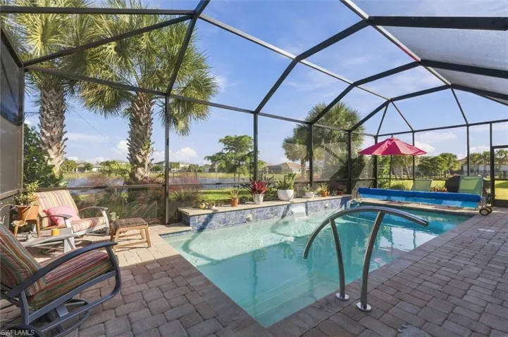 Screened-in lanai featuring a swimming pool with a tile-accented water feature, brick paver patio, and metal pool handrail