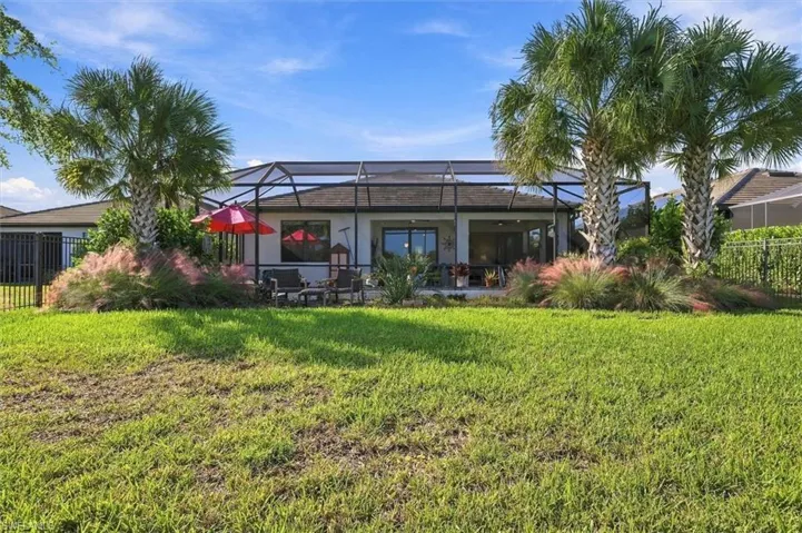 Backyard featuring a manicured lawn, metal-frame screened enclosure, mature palm trees, and ornamental shrubbery