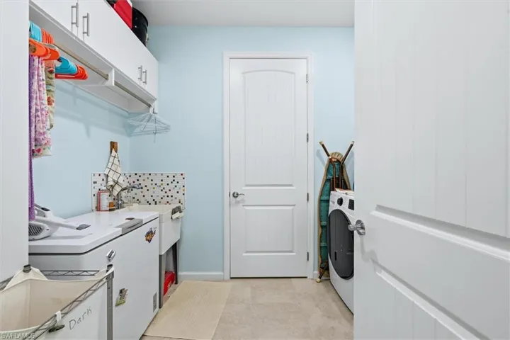 Utility room featuring overhead white cabinetry, a built-in utility sink, decorative mosaic tile backsplash, and solid-core interior doors